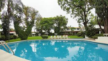 Una piscina rodeada de árboles y sillas de descanso.