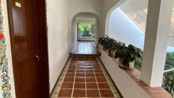 Un pasillo con suelo de baldosas, una puerta de madera y vistas a zonas verdes a través de un arco.