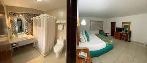Una habitación de hotel con baño, una cama con cubrecama verde, una mesita de noche y una ventana con persianas.