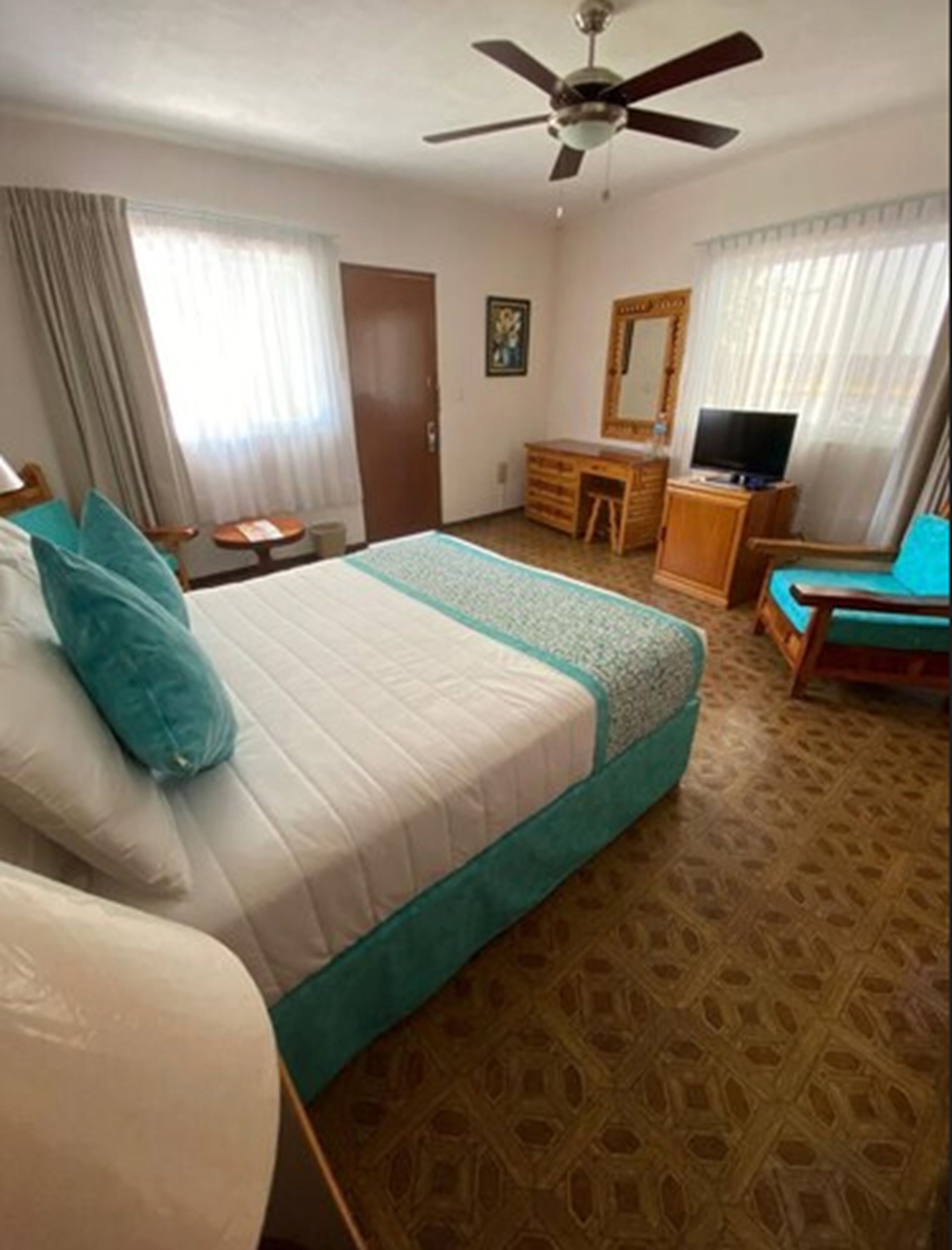 Une chambre d’hôtel équipée d’un lit, d’un bureau, d’une chaise, d’une télévision et d’un ventilateur de plafond.