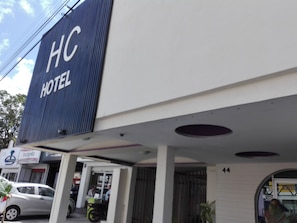 A hotel sign with "HC HOTEL" and a building entrance with a covered area and a car parked outside.