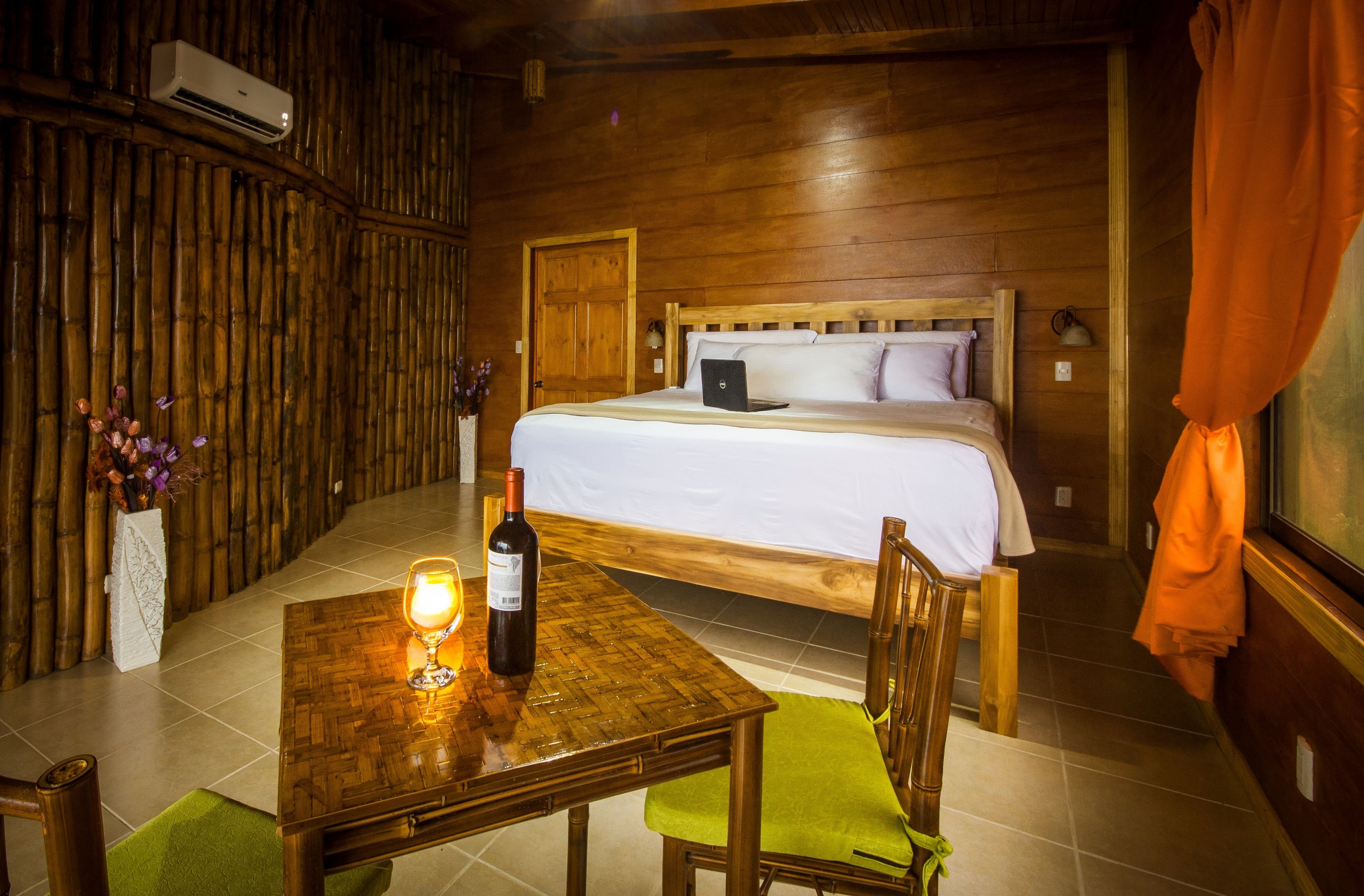 A wooden room with a bed, a table with a bottle of wine, and a chair.