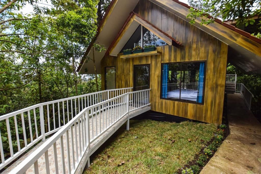 A wooden cabin with a white balcony, surrounded by greenery.