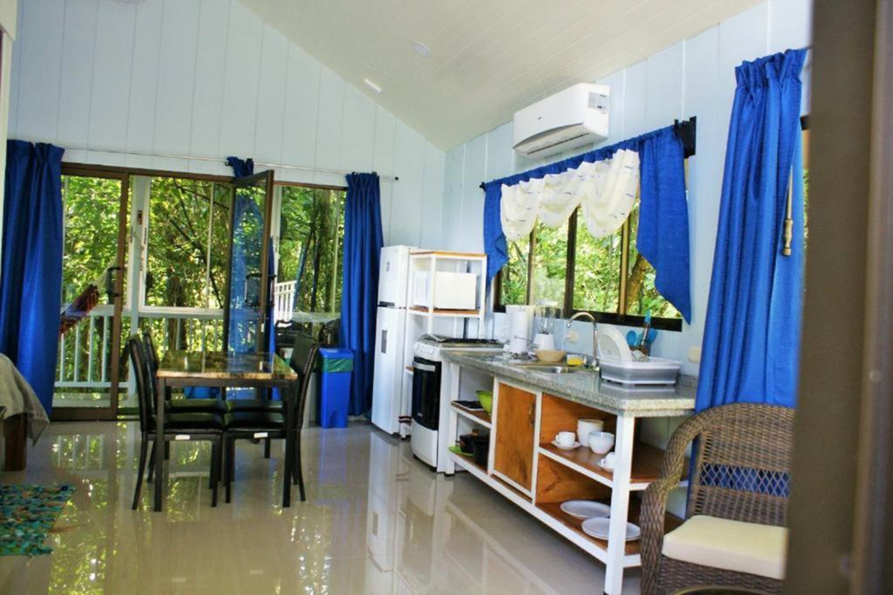 A compact kitchen with a dining area, large windows, and a view of greenery.