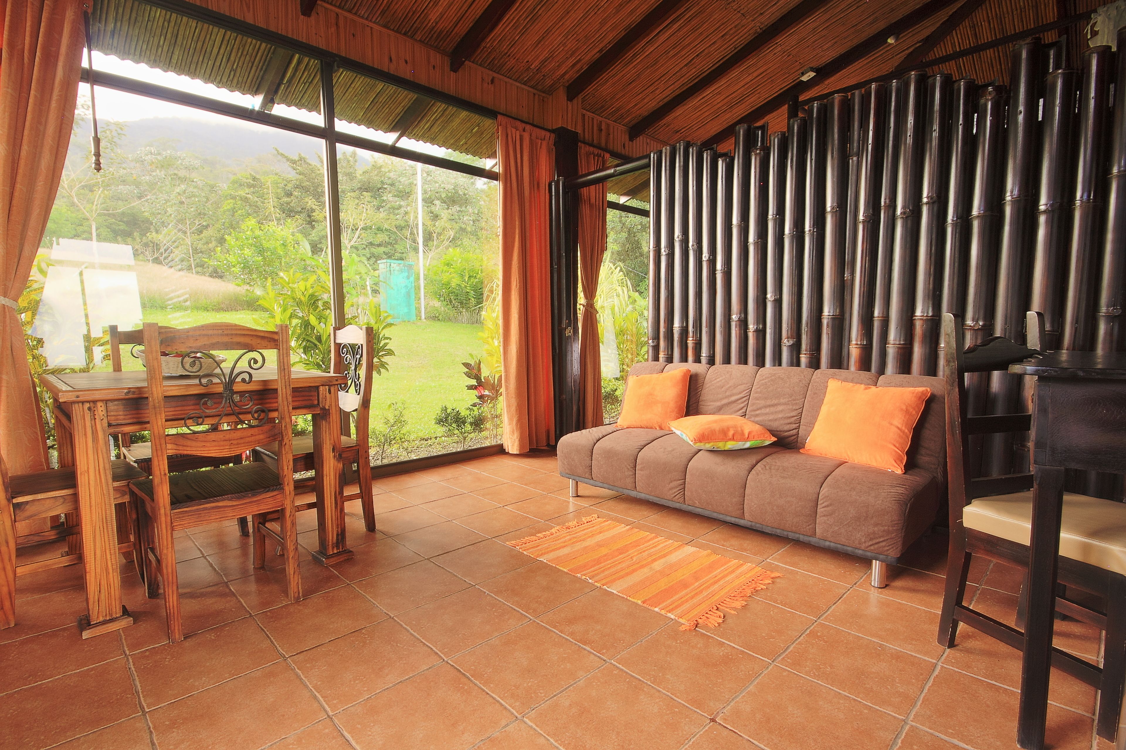 Una sala de estar con una mesa de madera, un sofá con cojines naranja y vistas al exterior.