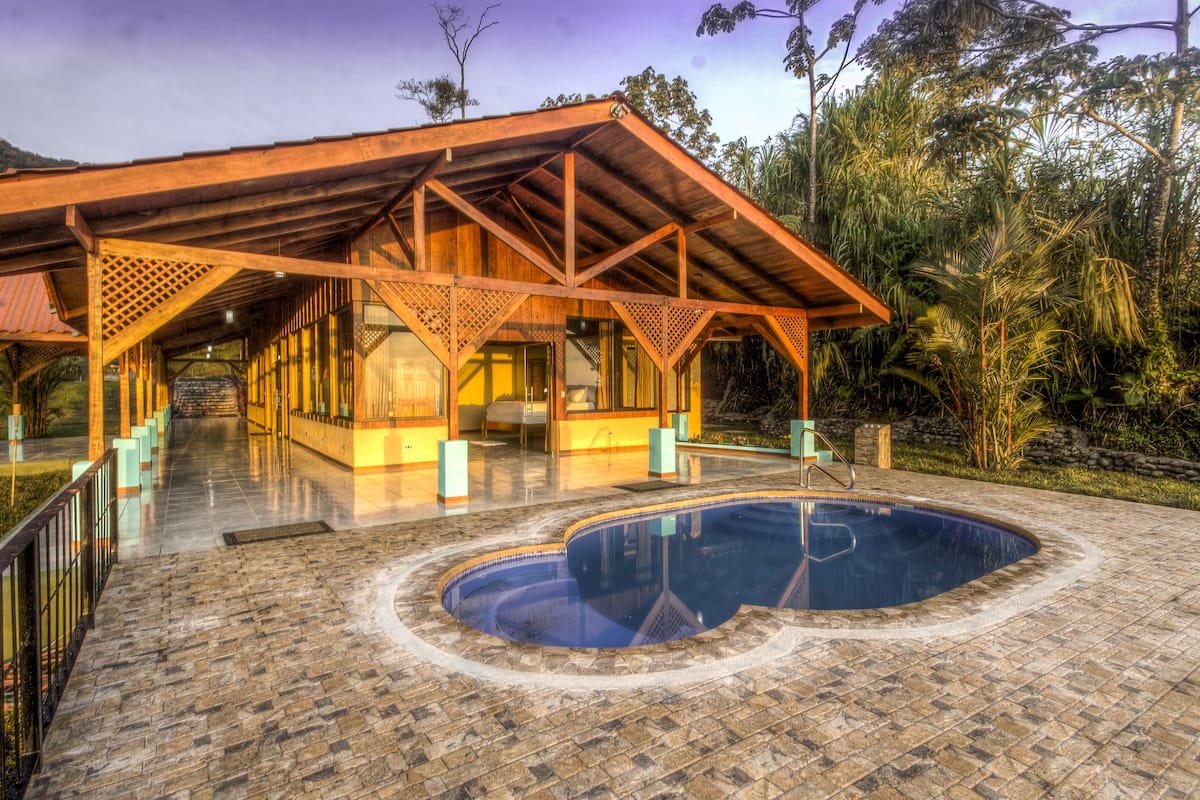 A resort with a pool, wooden deck, and a covered area with a view of the surrounding forest.