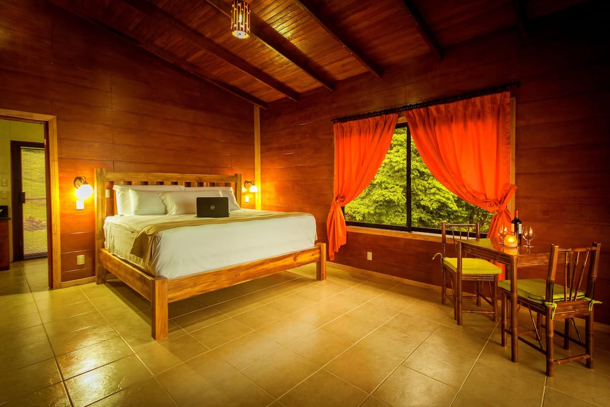 A wooden room with a bed, a table with chairs, and a window with curtains.