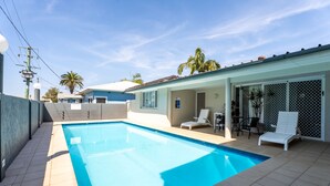 A swimming pool with a tiled deck, a covered patio area with seating, and a view of a residential building in the background. - Port Aloha Motel (Port Macquarie)
