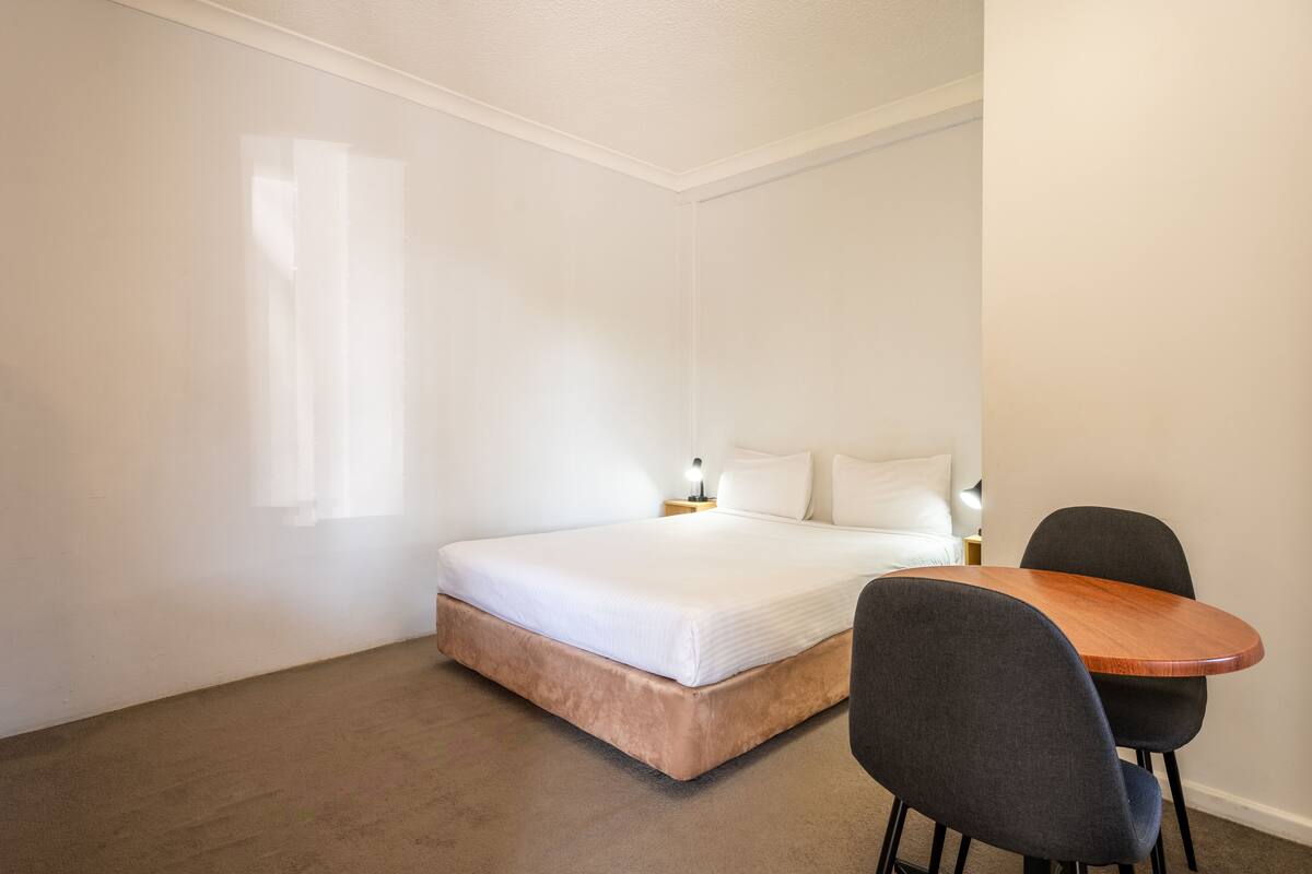 A bedroom with a bed, bedside table, lamp, and a small table with two chairs.