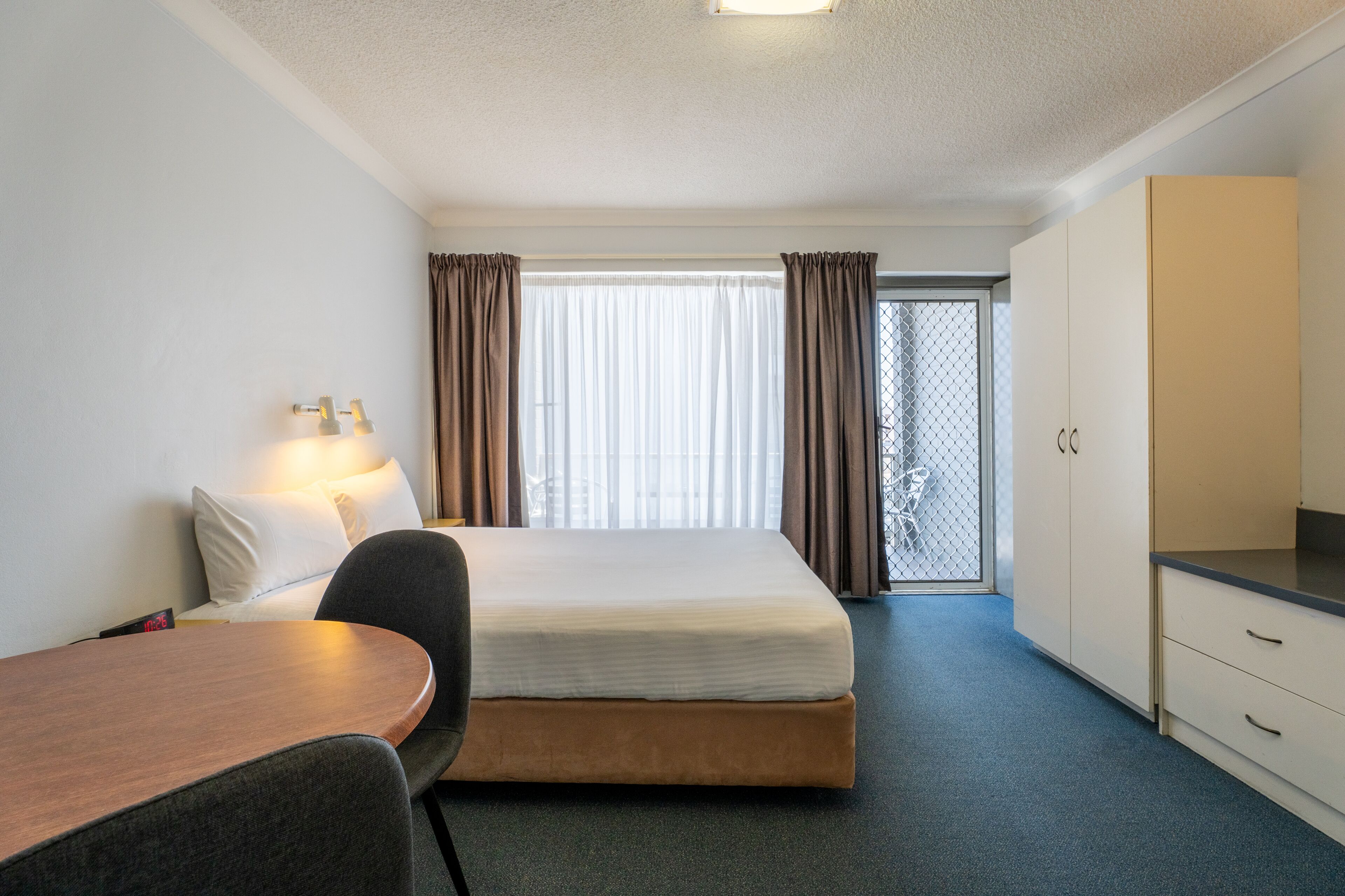 A hotel room with a bed, a desk, a chair, a wardrobe, and a window with curtains.
