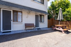 A building with a patio area featuring a wooden bench and picnic table. - Port Aloha Motel (Port Macquarie)