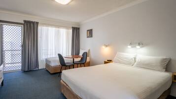 Une chambre d’hôtel avec un grand lit, un bureau avec deux chaises, une petite table et une fenêtre avec des rideaux.