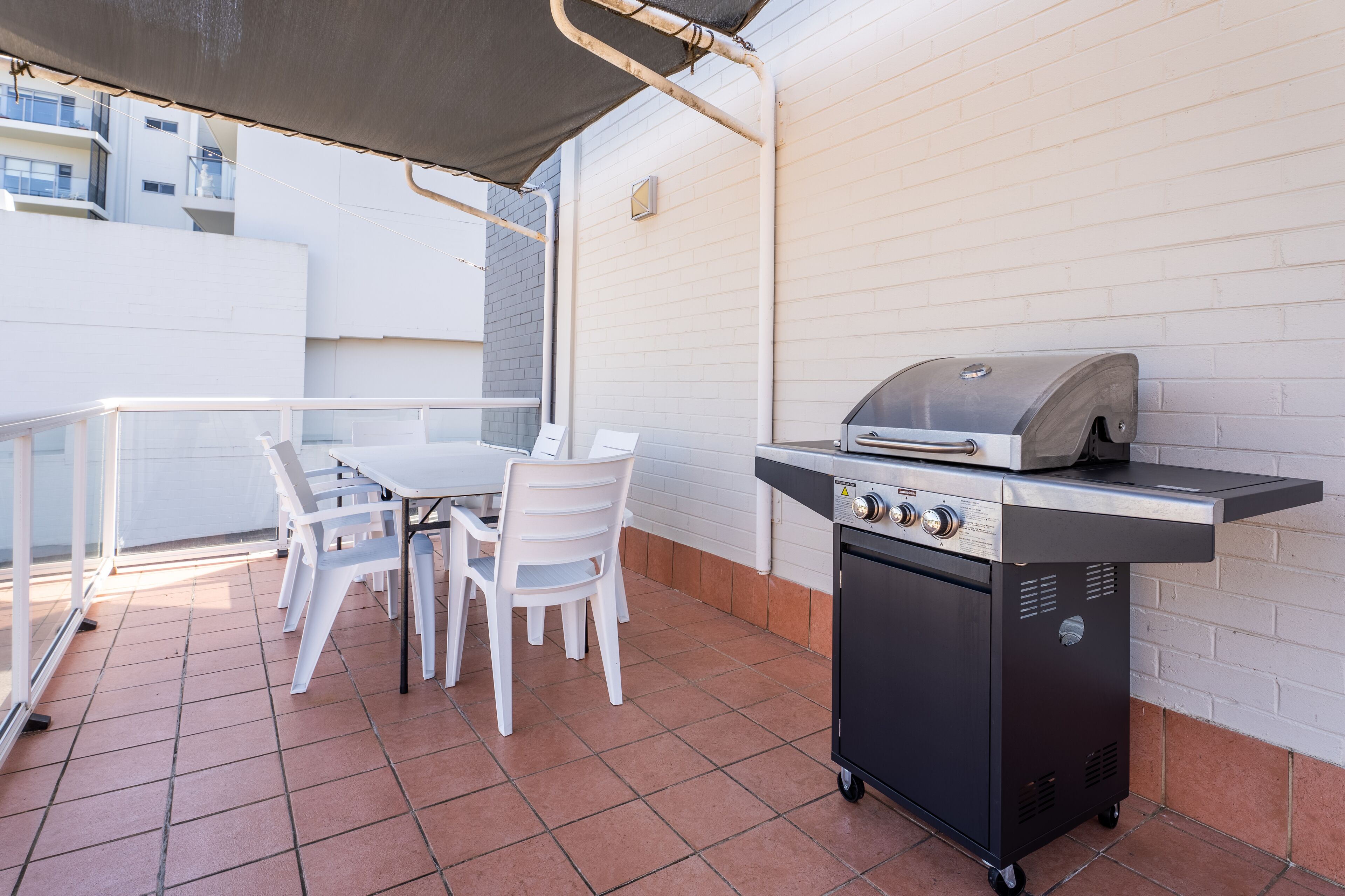 An outdoor patio with a grill, white chairs, and a table.