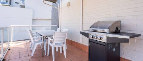 An outdoor patio with a grill, white chairs, and a table.
