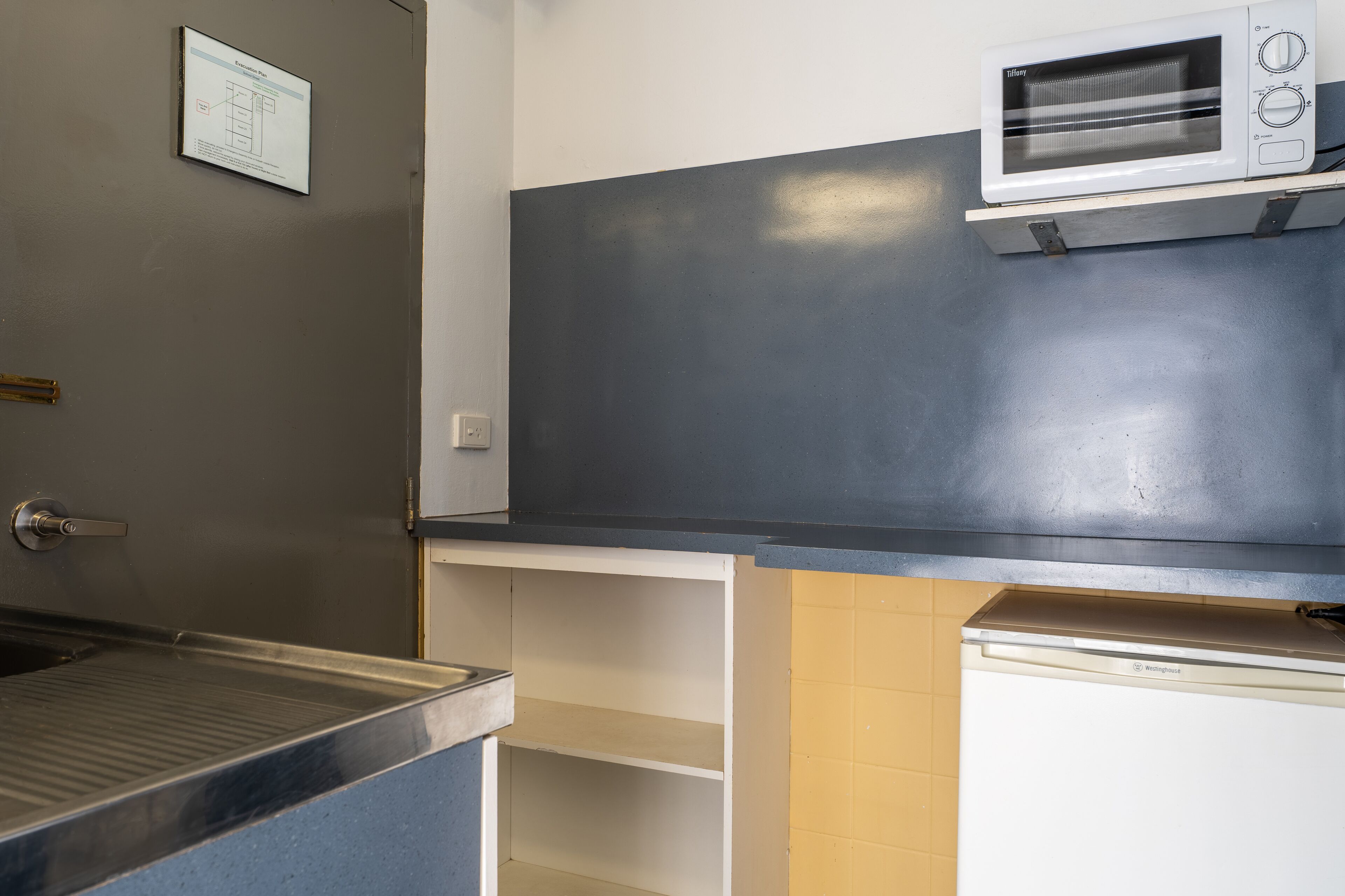 A kitchenette with a microwave, a sink, and a stainless steel countertop.