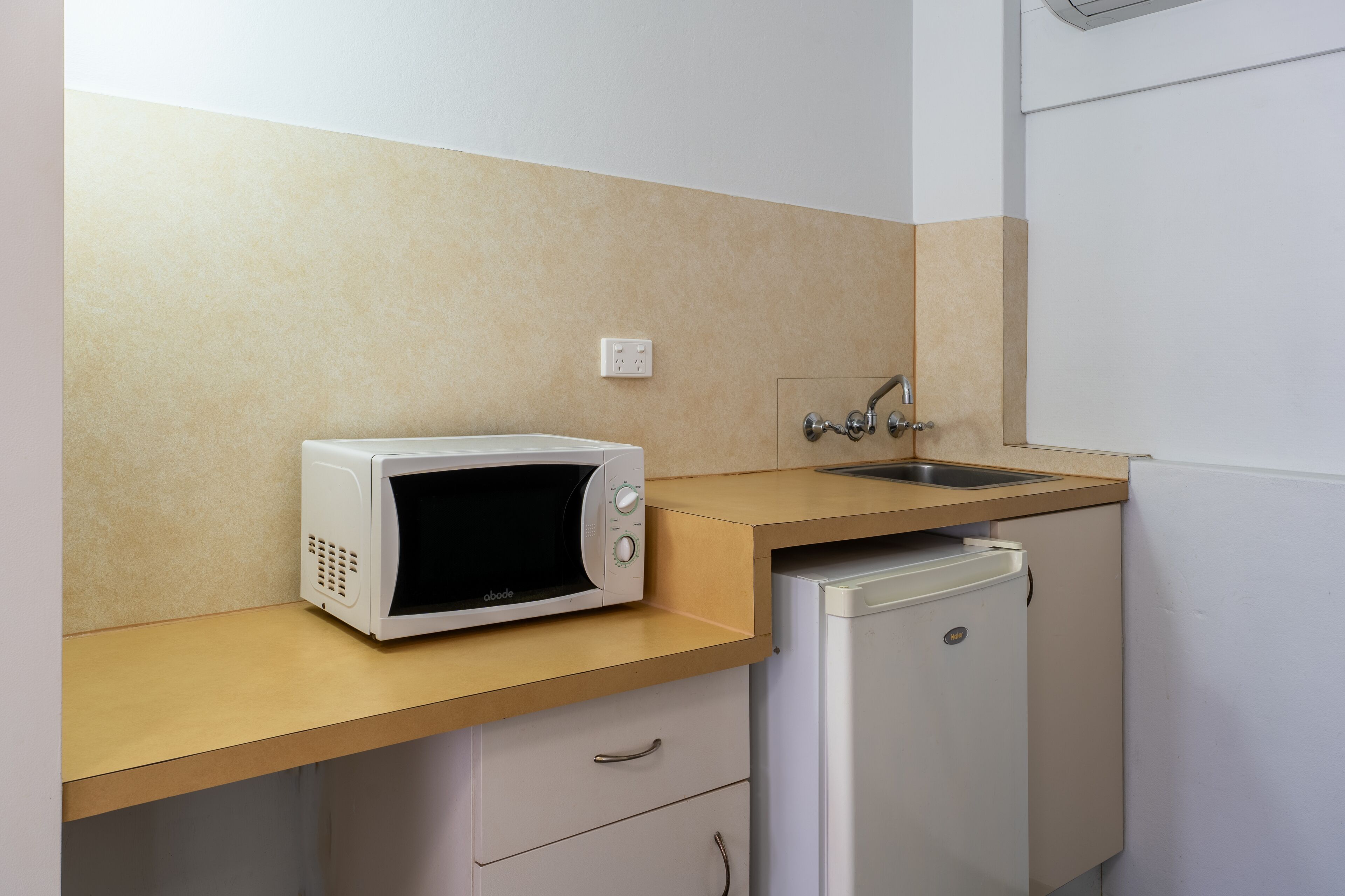 Una cocina con microondas, lavamanos y un refrigerador pequeño.