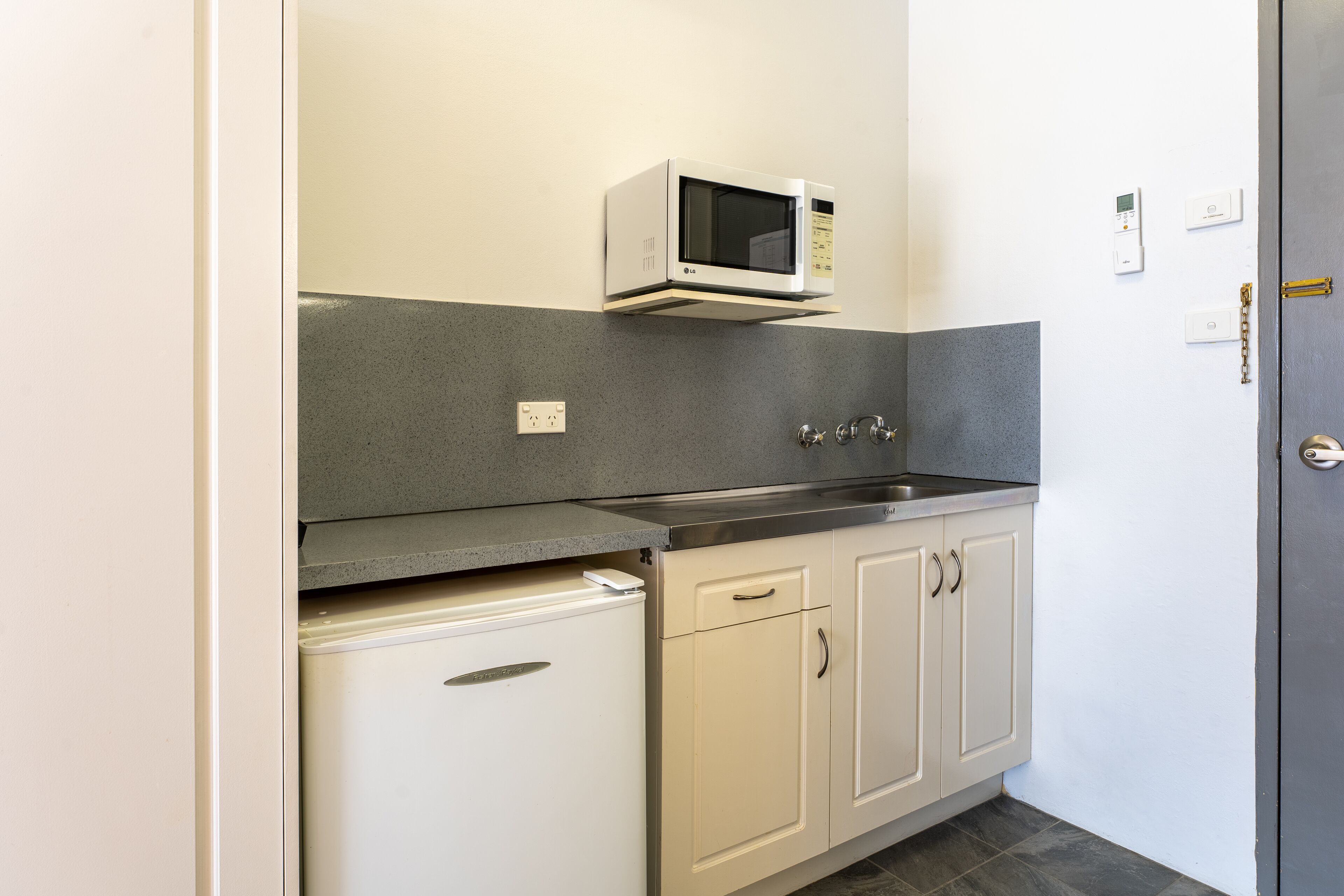 A compact kitchen with a built-in microwave, a small refrigerator, and a sink.