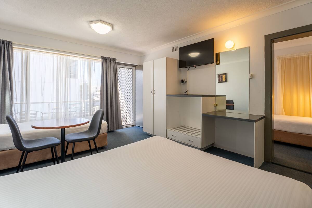 A hotel room with a bed, a desk, a chair, a small table, and a balcony with a view.