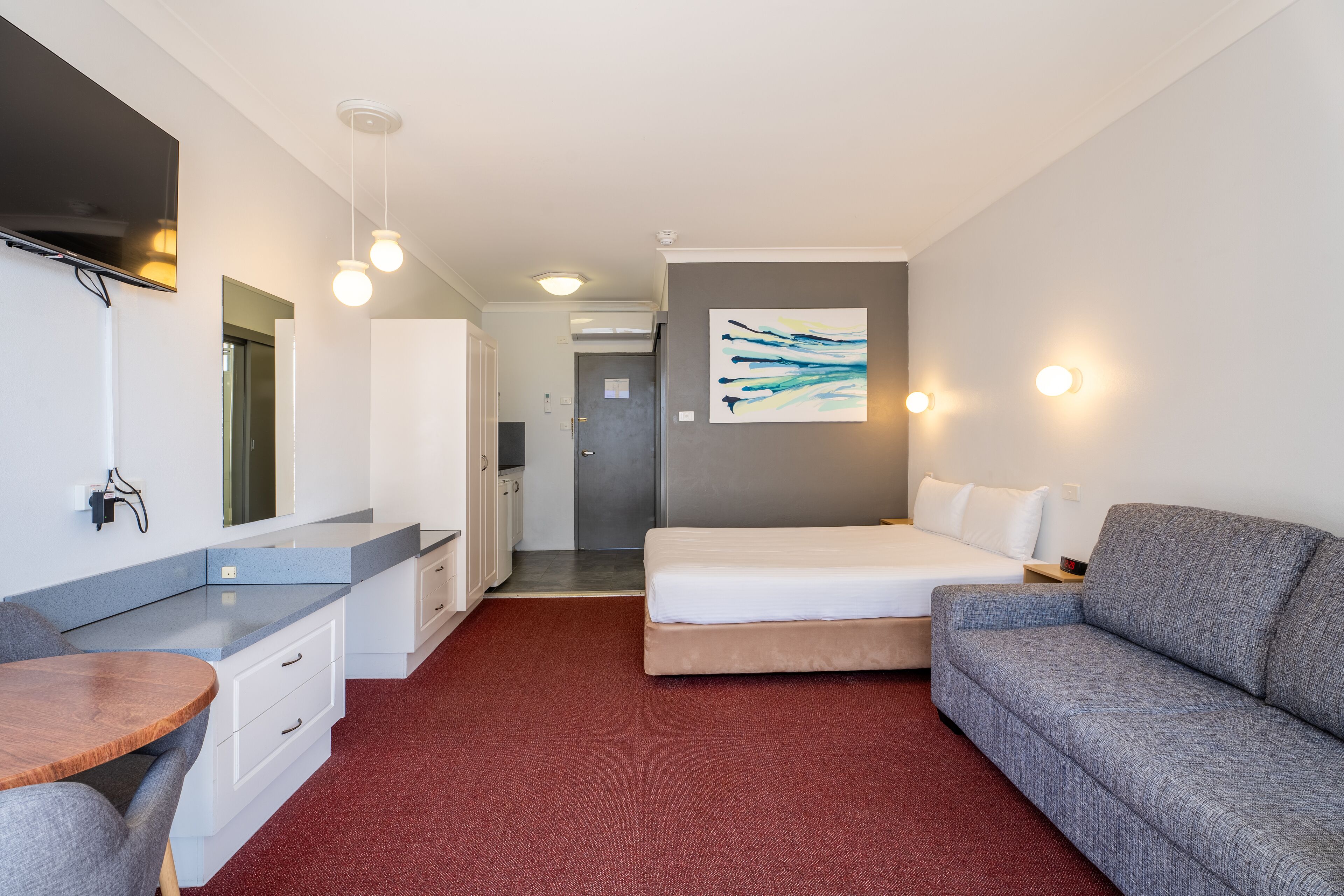 A modern hotel room with a bed, a sofa, a desk, and a kitchenette.