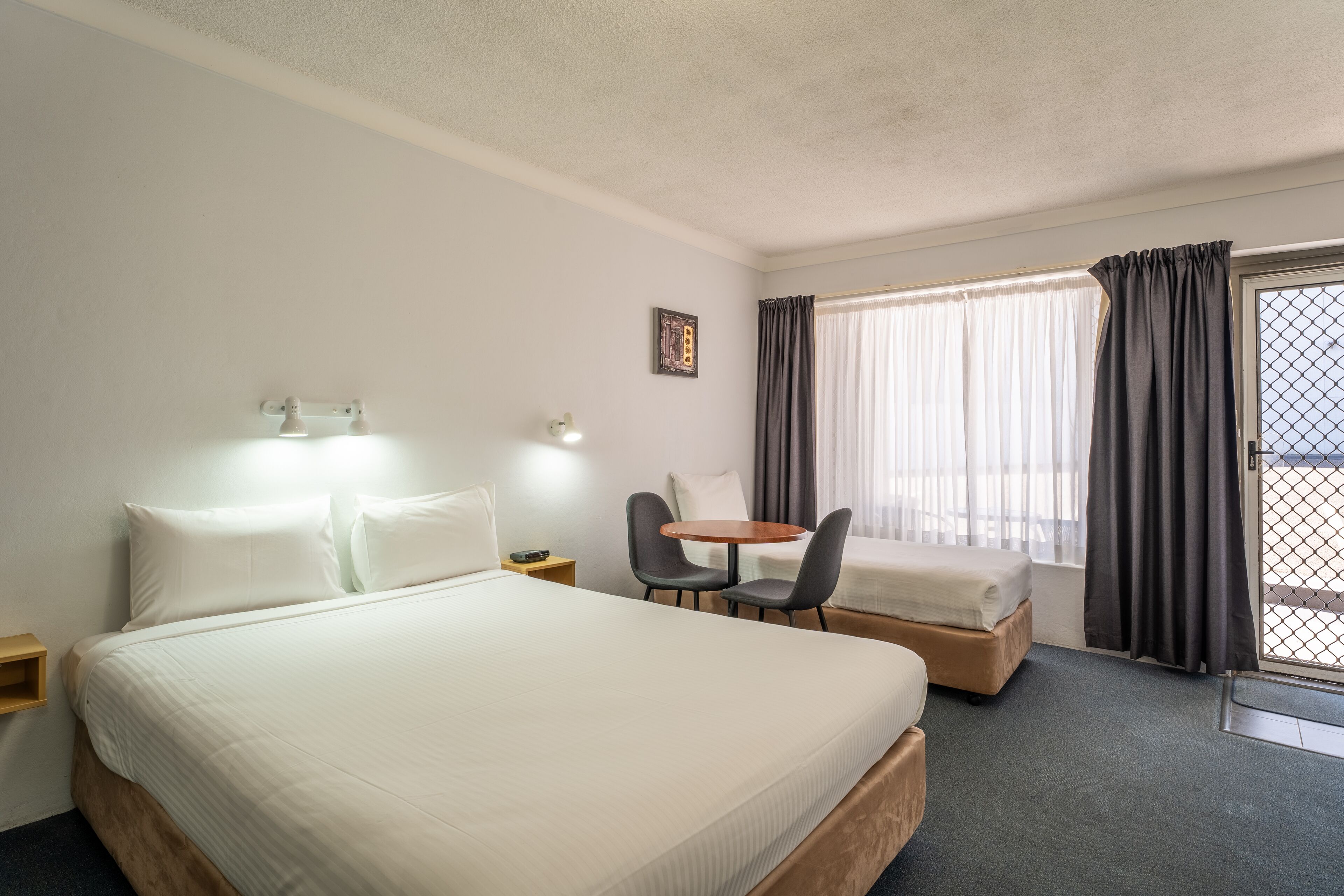A hotel room with a large bed, a small table with two chairs, a desk, and a window with curtains.