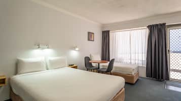 A hotel room with a large bed, a small table with two chairs, a desk, and a window with curtains.