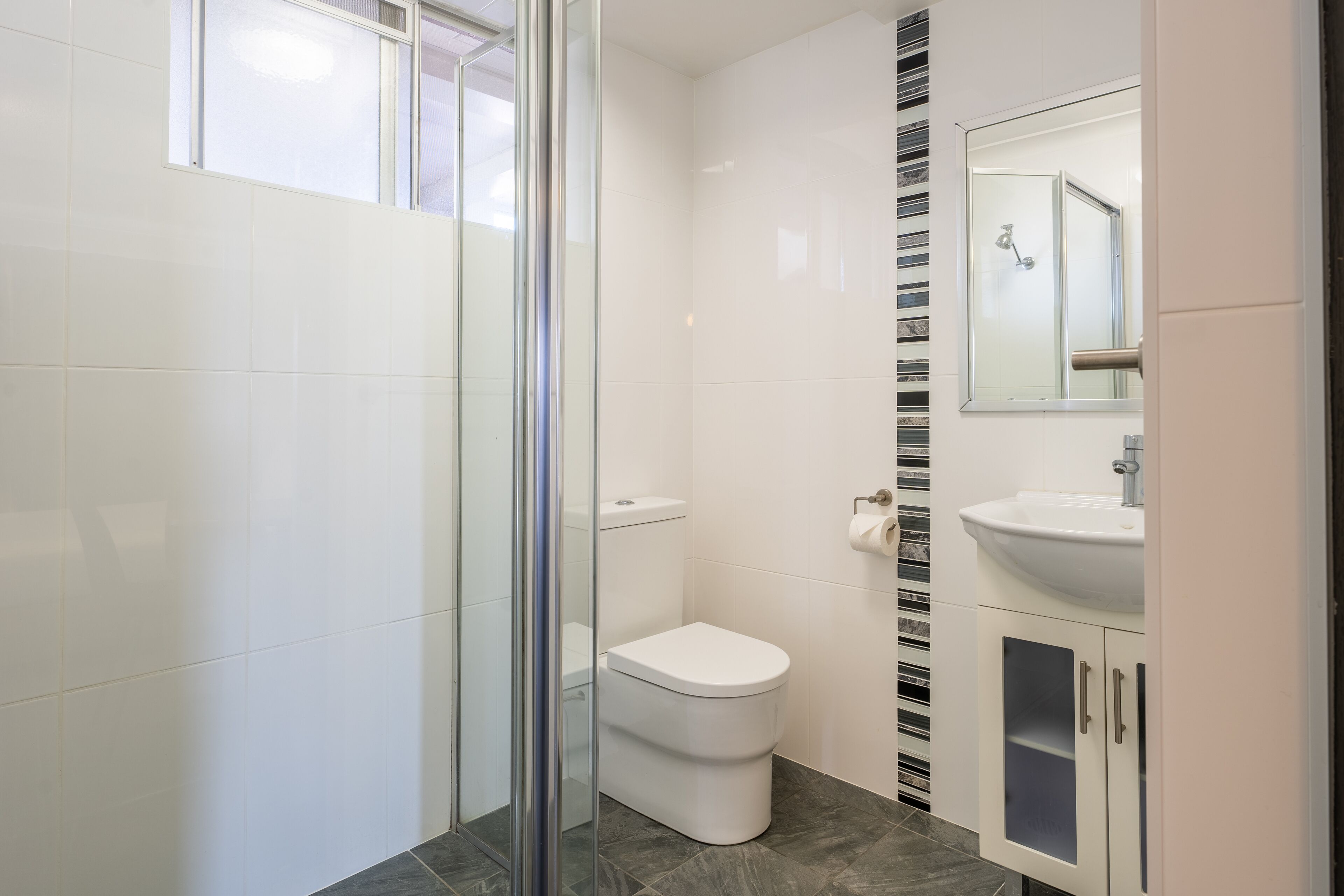 Ein modernes Badezimmer mit Duschkabine aus Glas, einer weißen Toilette und einem Waschtisch mit Spiegel und Spüle.
