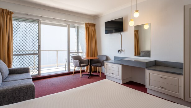 A hotel room with a bed, a desk with a chair, a TV, a mirror, and a window with curtains. - Port Aloha Motel (Port Macquarie)