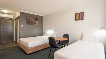 A hotel room with two beds, a small table, chairs, a door, and a wall-mounted artwork.