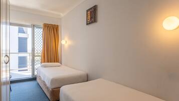 A hotel room with two beds, a sliding glass door to the balcony, and a wall-mounted light fixture.