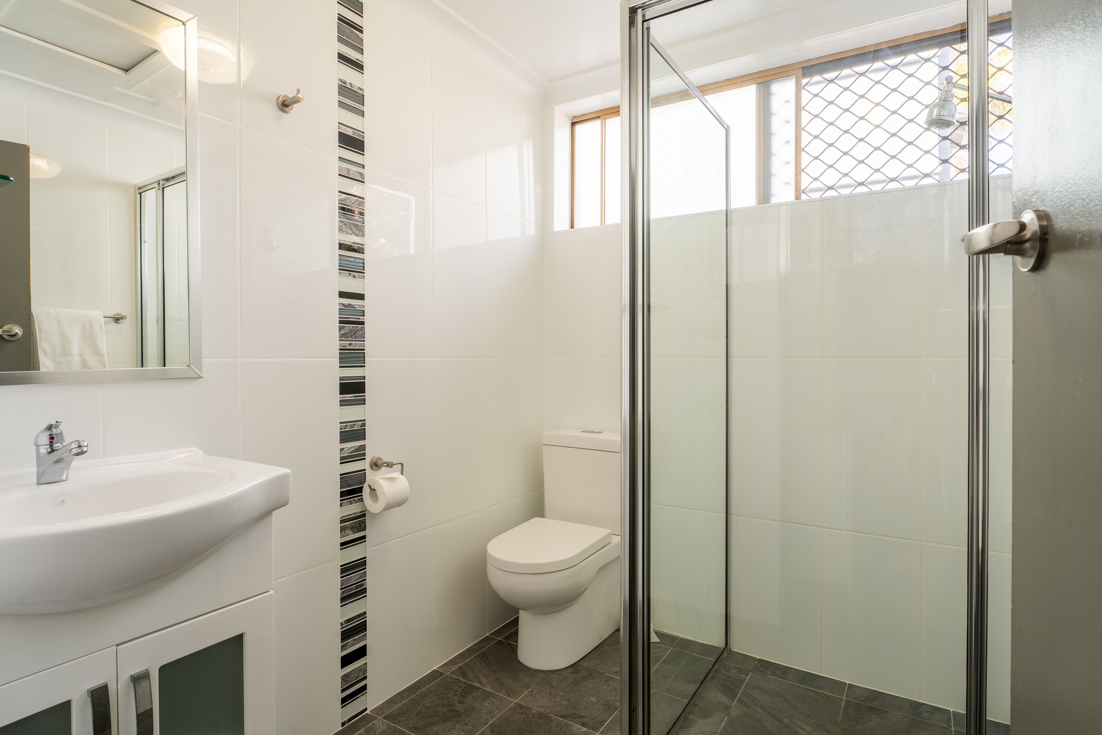 A bathroom with a glass-enclosed shower, a white sink, and a toilet.