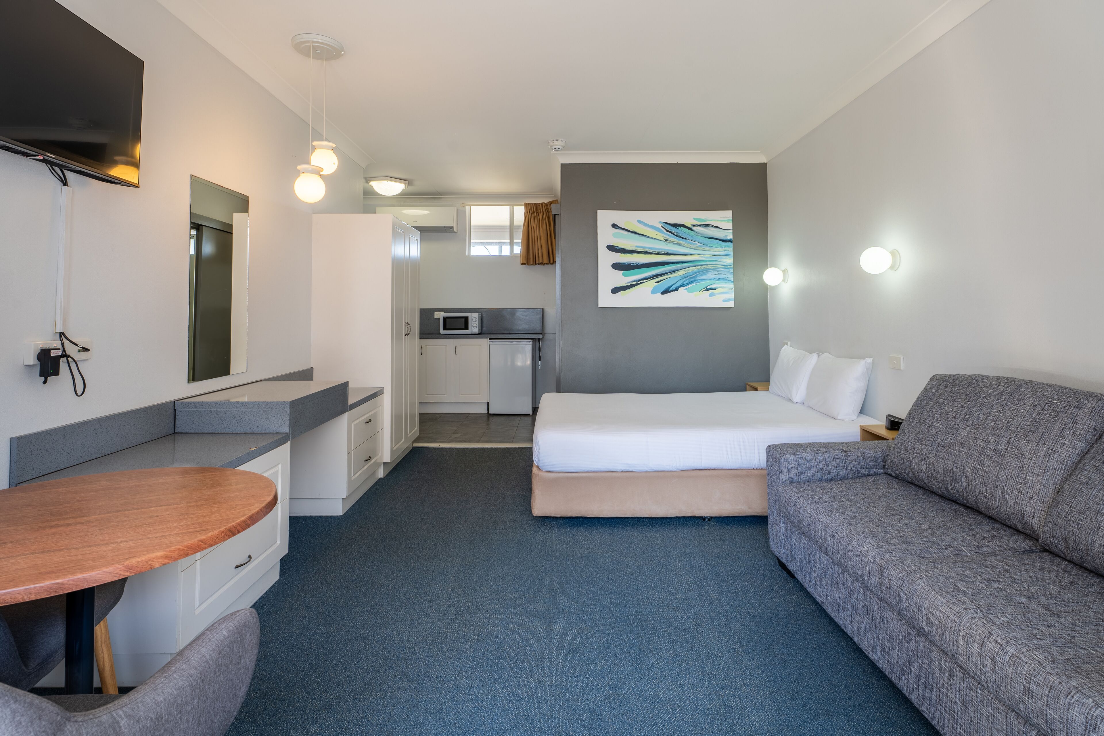 A modern hotel room with a bed, a sofa, a desk, and a kitchenette.