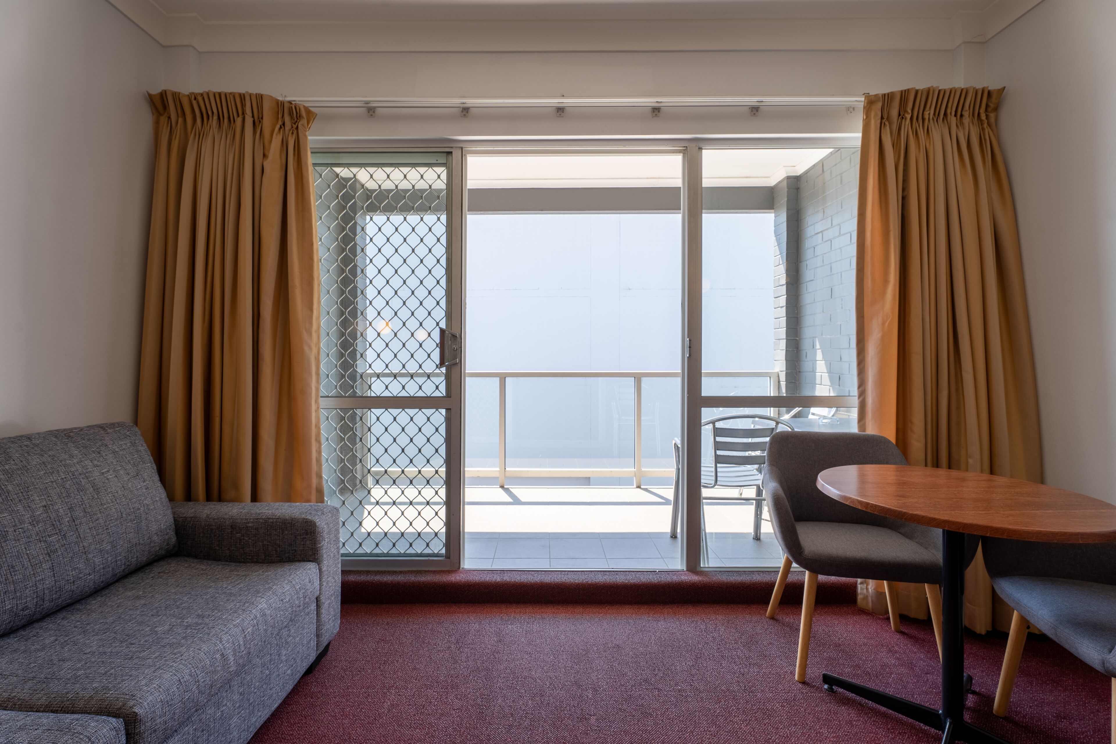 A hotel room with a sofa, a dining table, and a balcony with a view.