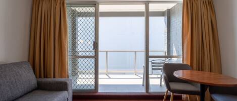 A hotel room with a sofa, a dining table, and a balcony with a view.