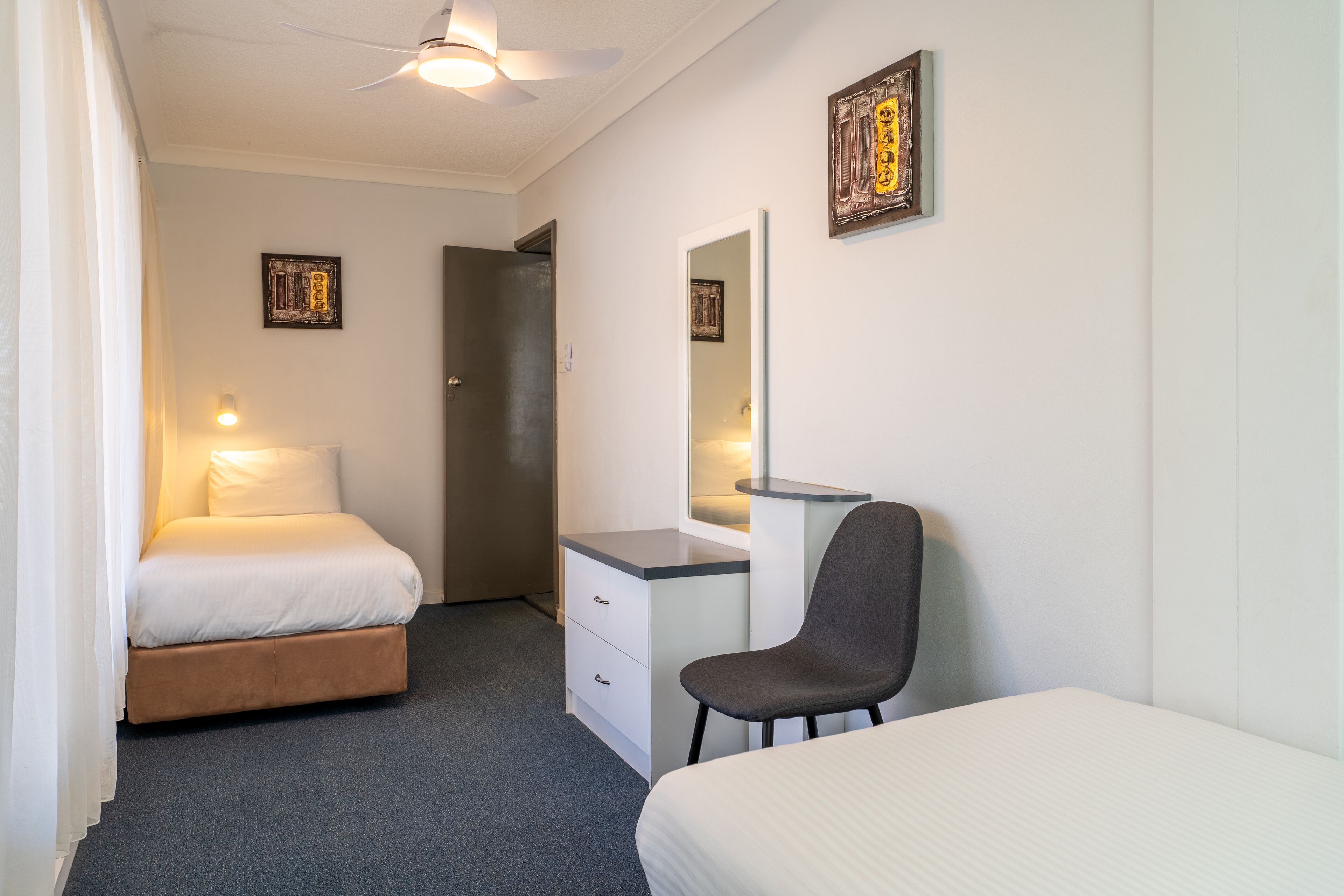 A hotel room with a bed, a desk, a chair, a mirror, and two wall-mounted picture frames.
