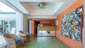 A hotel lobby with wicker chairs, a reception desk, a wall of magazines, and a view through an open door. - Port Aloha Motel (Port Macquarie)