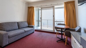 A room with a grey sofa, a small round table with two chairs, a desk with drawers, and a sliding glass door with curtains. - Port Aloha Motel (Port Macquarie)