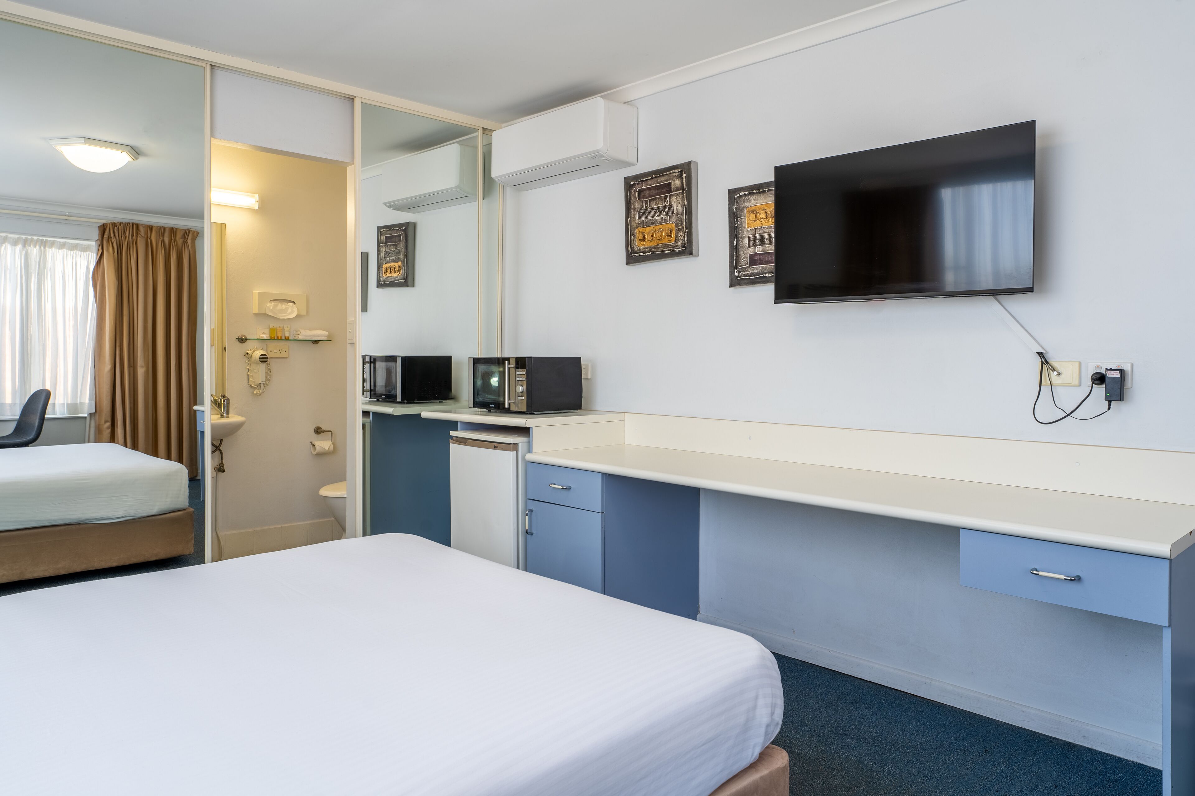 Hotellihuone, jossa on sänky, työpöytä, peili, televisio ja pieni keittokomero.