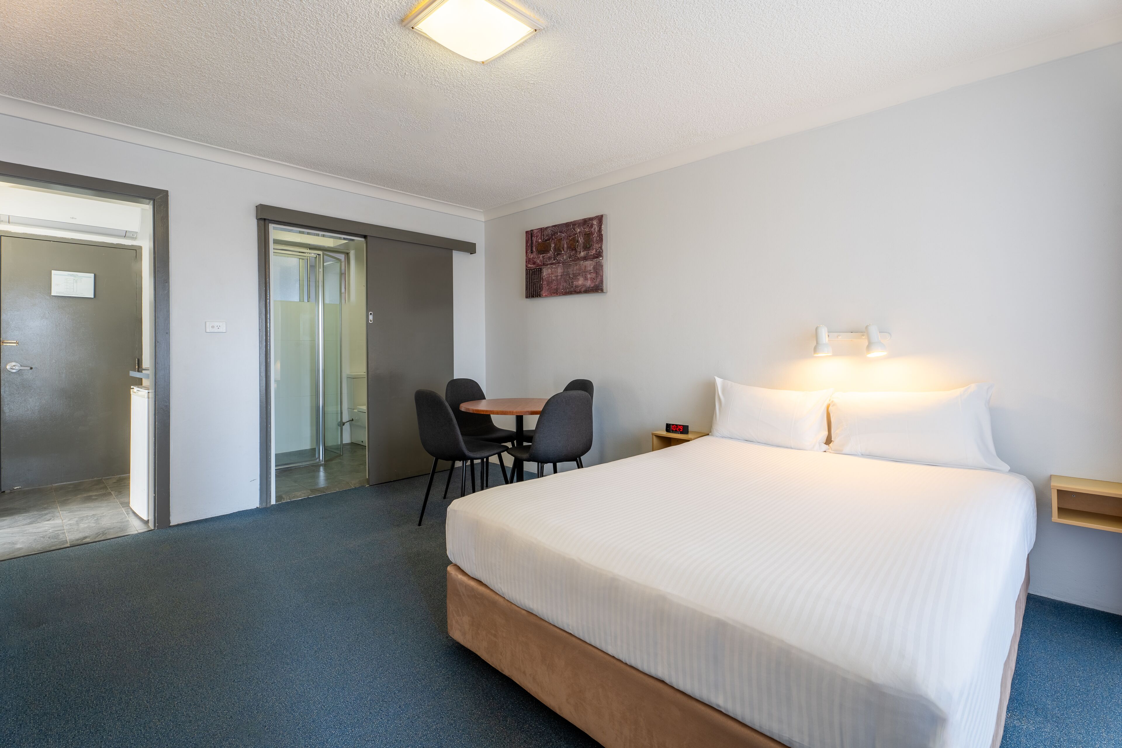 Une chambre d’hôtel avec un grand lit, un bureau avec deux chaises, une petite table et une table de chevet avec une lampe.