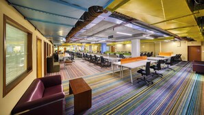 A conference room with multiple tables and chairs, a patterned carpet, and a ceiling with exposed ductwork. - Featherlite Evoma Hotel (Bengaluru)