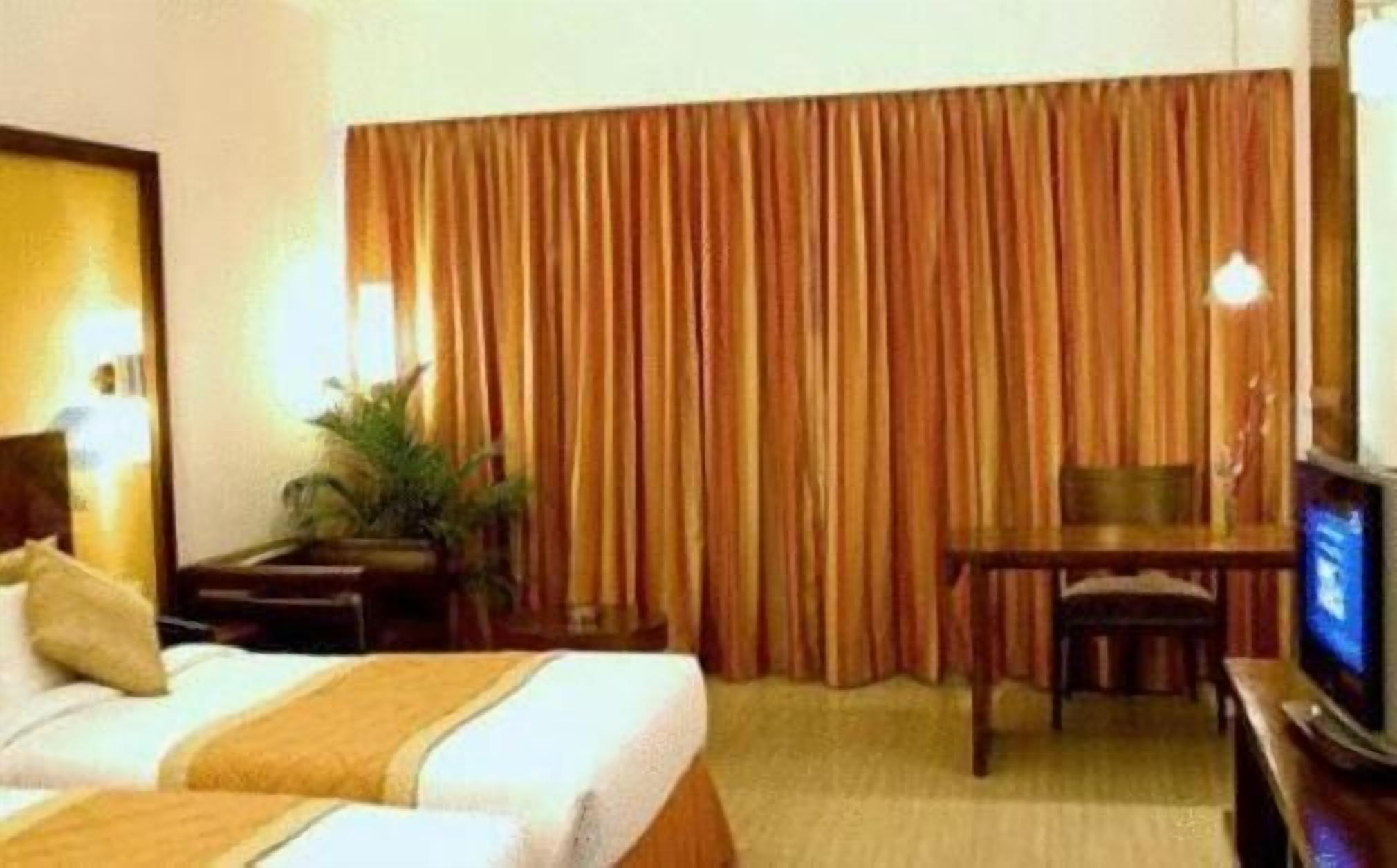 Una camera d'albergo con due letti, una scrivania, una sedia, un televisore e una tenda.
