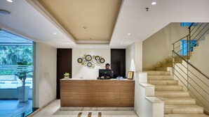 A reception area with a wooden counter, a modern ceiling design, and a staircase to the right. - Featherlite Evoma Hotel (Bengaluru)