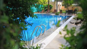 A swimming pool with metal ladders, surrounded by lounge chairs and potted plants. - Featherlite Evoma Hotel (Bengaluru)