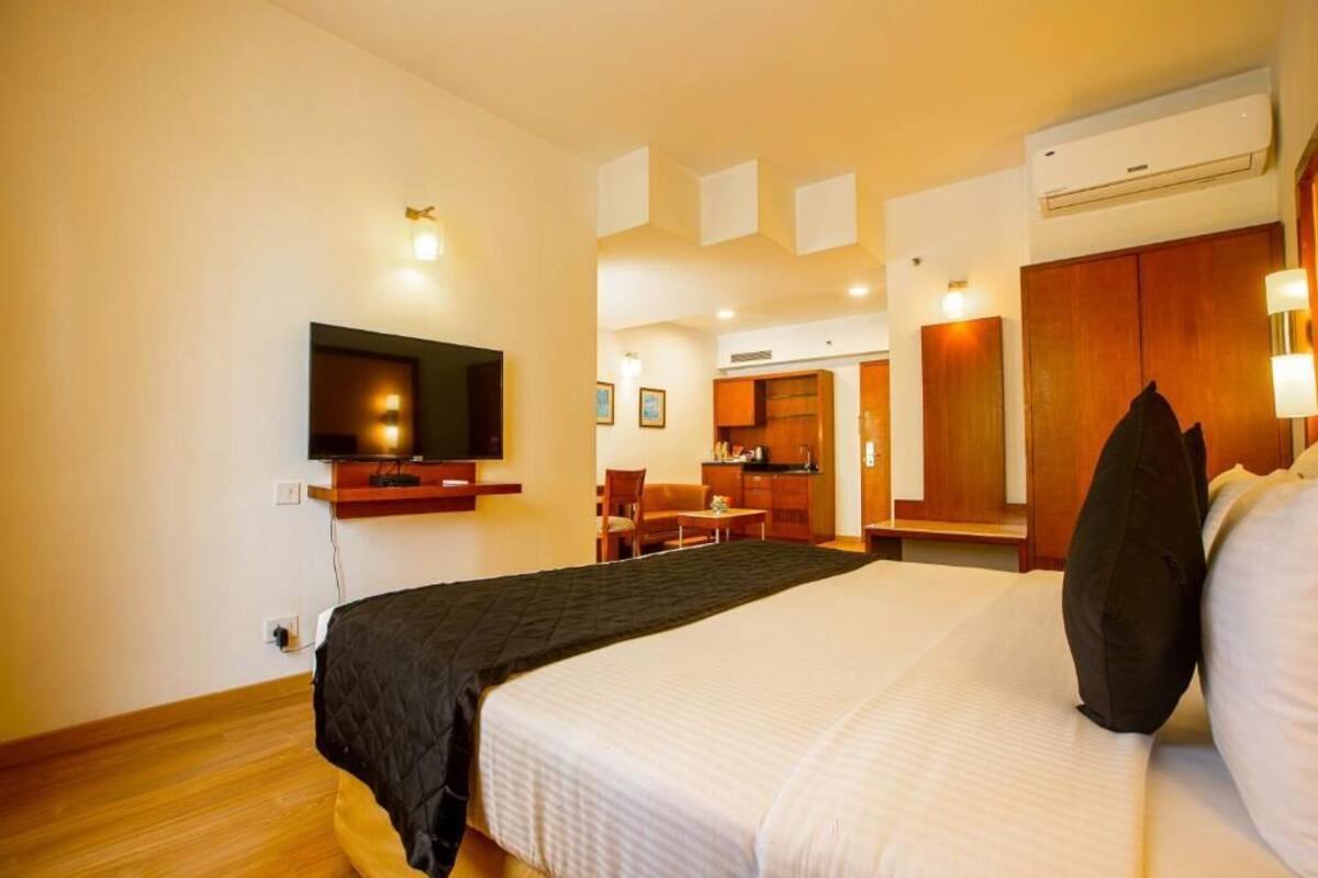 Una habitación de hotel con una cama, un televisor montado en la pared, una kitchenette y un armario de madera.