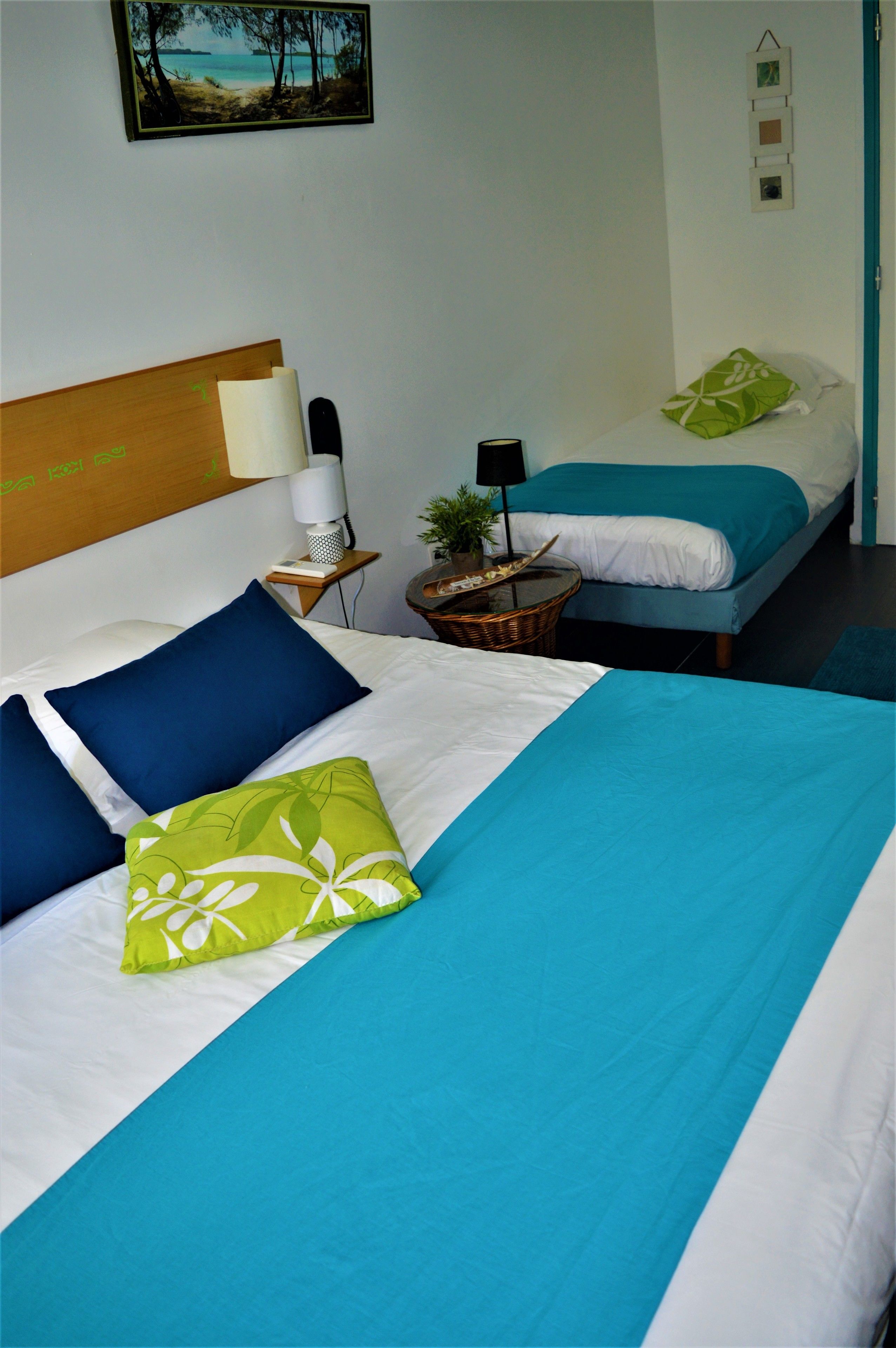 Une chambre d’hôtel avec deux lits, chacun ayant une literie de couleur différente. On y trouve une table de chevet avec une lampe et une petite table sur laquelle est posée une plante.