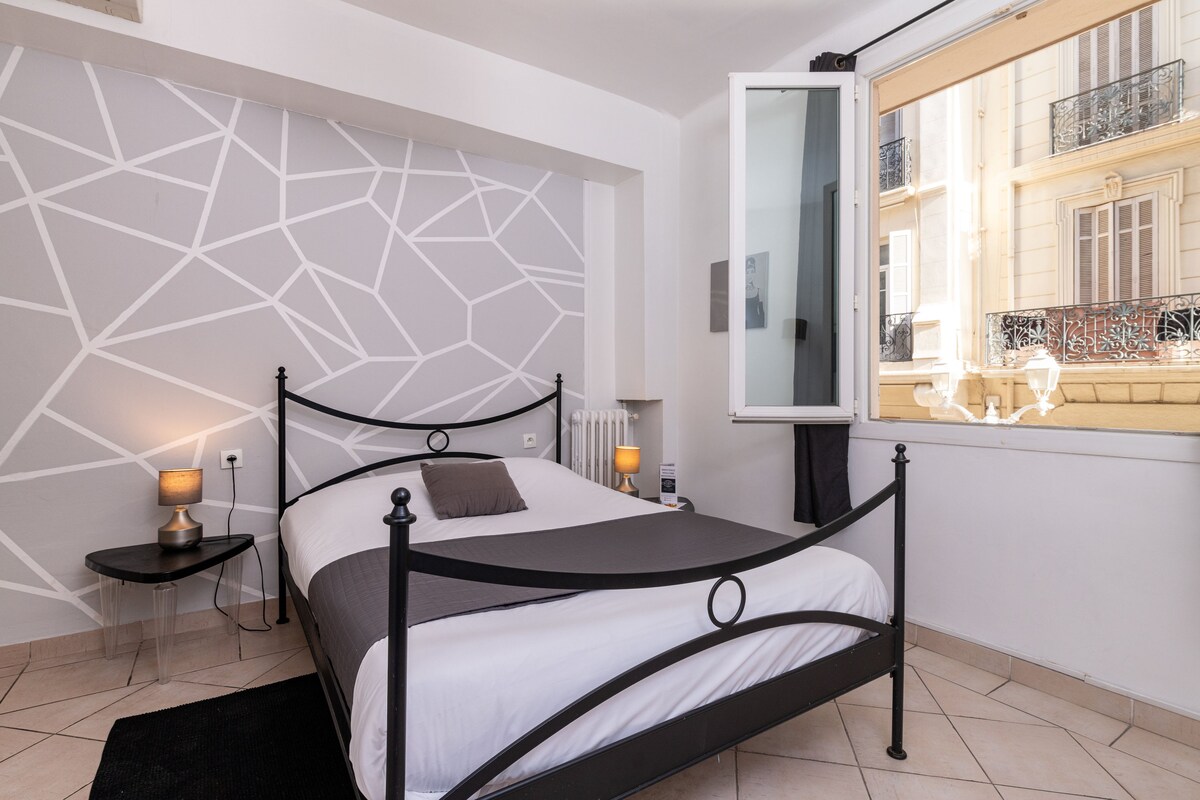 A modern bedroom with a geometric-patterned wall, a black metal bed frame, and a view of a balcony with a railing.