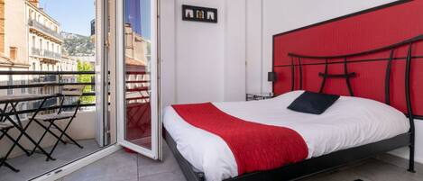 A bedroom with a bed, a red headboard, a balcony with a table and chairs, and a city view.