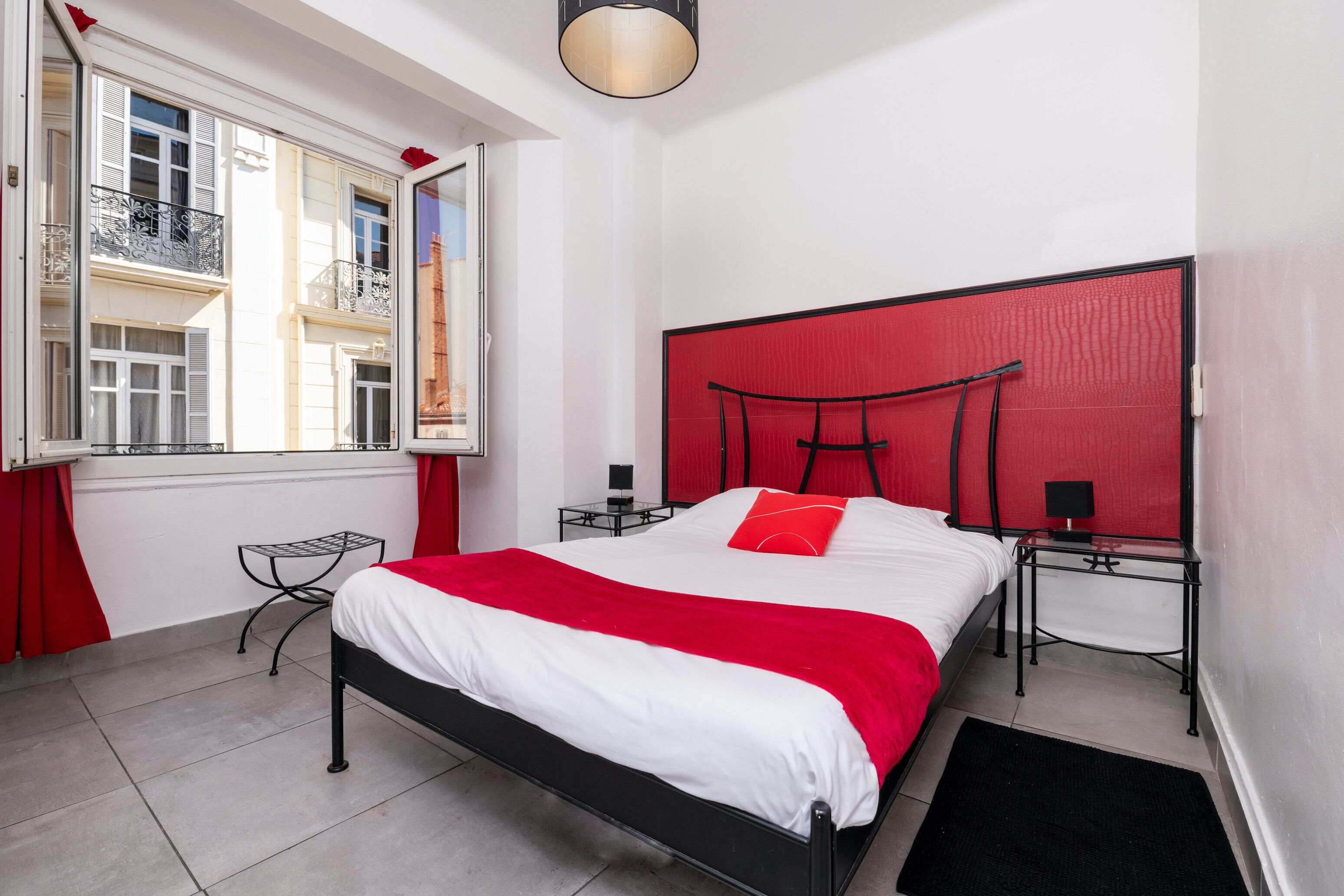 Camera da letto moderna con struttura letto in metallo nero, biancheria da letto bianca e una parete di colore rosso.
