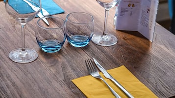A table with wine glasses, a menu, and cutlery on a wooden table.