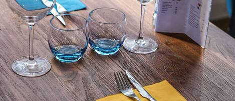 A table with wine glasses, a menu, and cutlery on a wooden table.