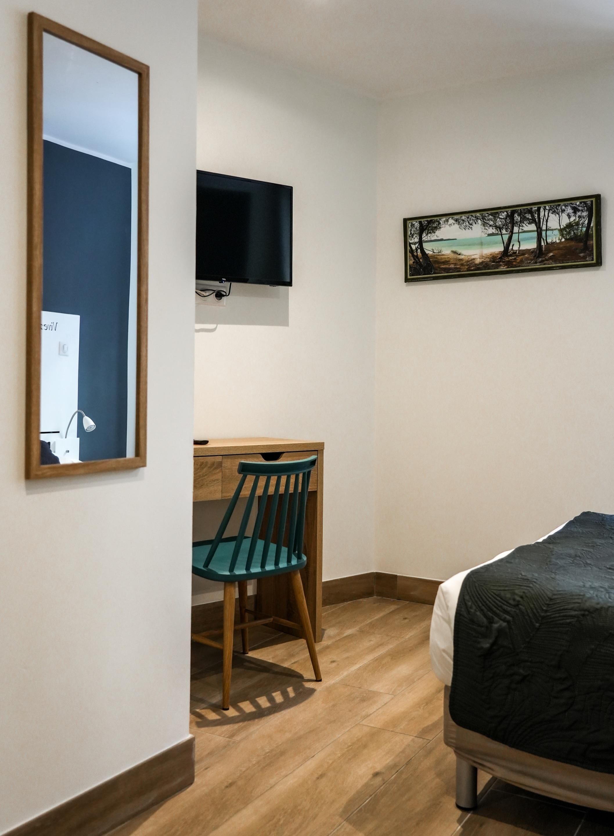 Een slaapkamer met een bed, een bureau met stoel, een aan de muur bevestigde televisie en een ingelijst kunstwerk.